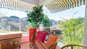 Un balcon agrémenté de meubles en osier, d’une grande plante en pot et offrant une vue sur la campagne.