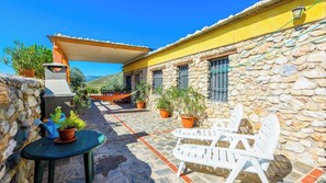 A stone building with a yellow facade, outdoor seating, and potted plants.