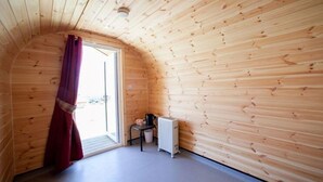 Ein kleiner Raum mit Holzvertäfelung, einer gewölbten Decke, einem Heizkörper, einem Sessel und einem Fenster mit Vorhang.