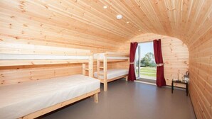 Ein Holzblockhaus-Innenraum mit Etagenbetten, einem kleinen Tisch und einem Fenster mit Vorhängen.