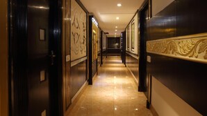Un pasillo con puertas de madera oscura, suelos de mármol y obras enmarcadas en las paredes.