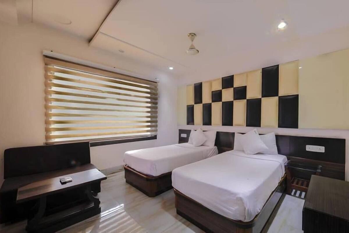 Quarto de hotel com duas camas, uma escrivaninha, televisão e uma janela grande com persianas.