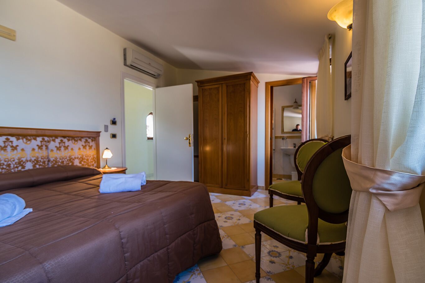 A hotel room with a bed, a chair, a desk, and a wardrobe.