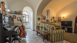 A living room with a grand piano, a cello, a patterned sofa, and a television. - Agriturismo Il Giardino di Vigliano (Massa Lubrense)