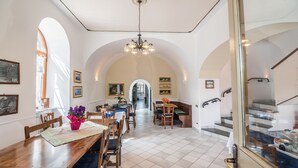 A spacious dining area with a wooden table and chairs, a chandelier, and a view of a staircase leading to an upper level. - Agriturismo Il Giardino di Vigliano (Massa Lubrense)