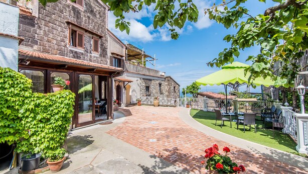 A courtyard with a stone building, potted plants, and outdoor furniture. - Agriturismo Il Giardino di Vigliano (Massa Lubrense)