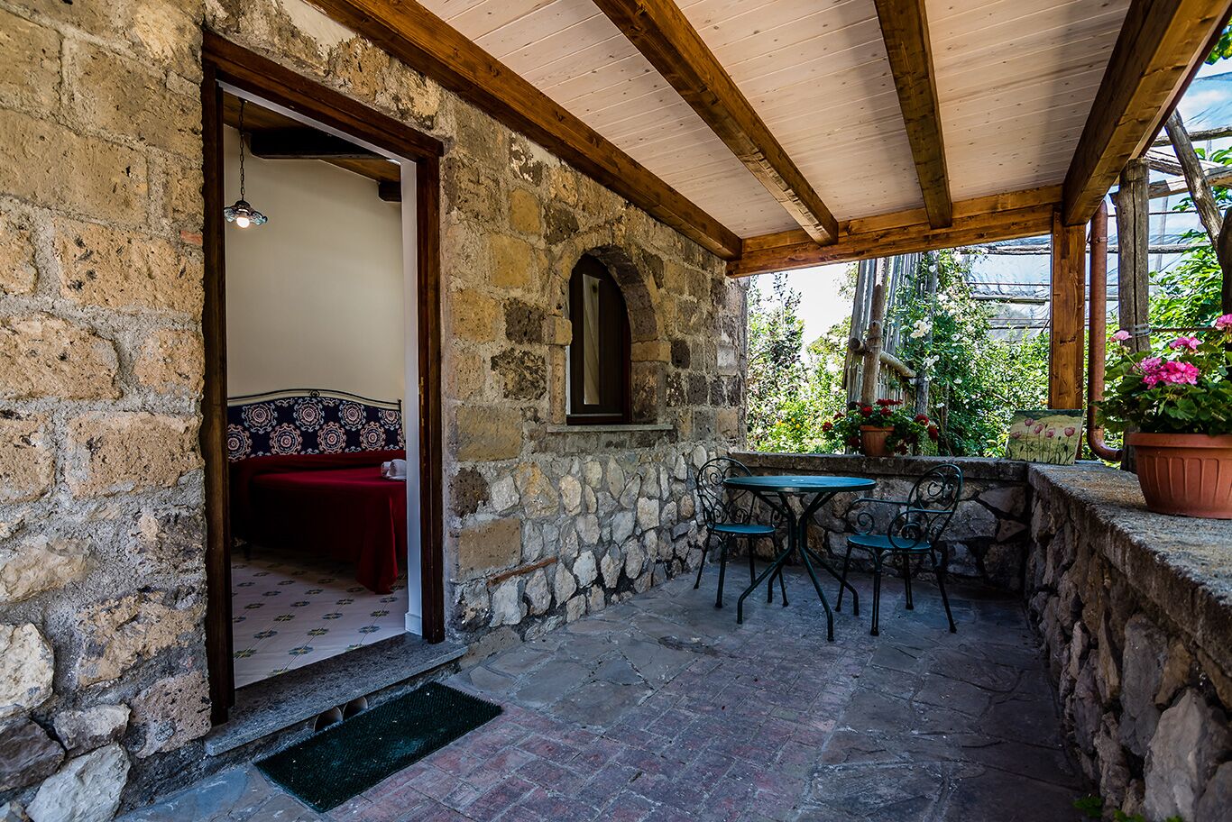 Una habitación con paredes de piedra, techo de madera, una cama con colcha estampada y una pequeña mesa con sillas.
