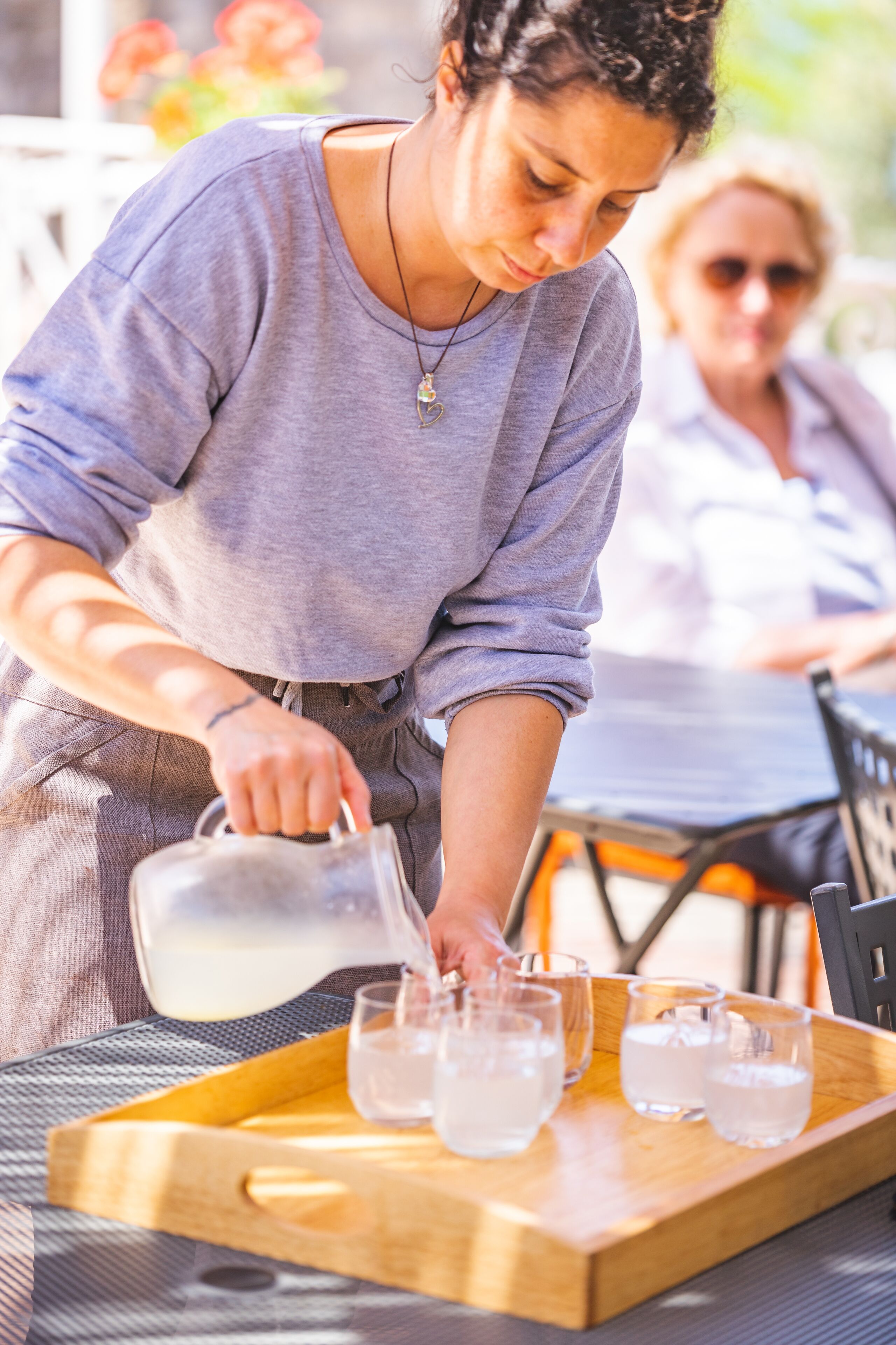 A person pouring water into glasses on a tray.