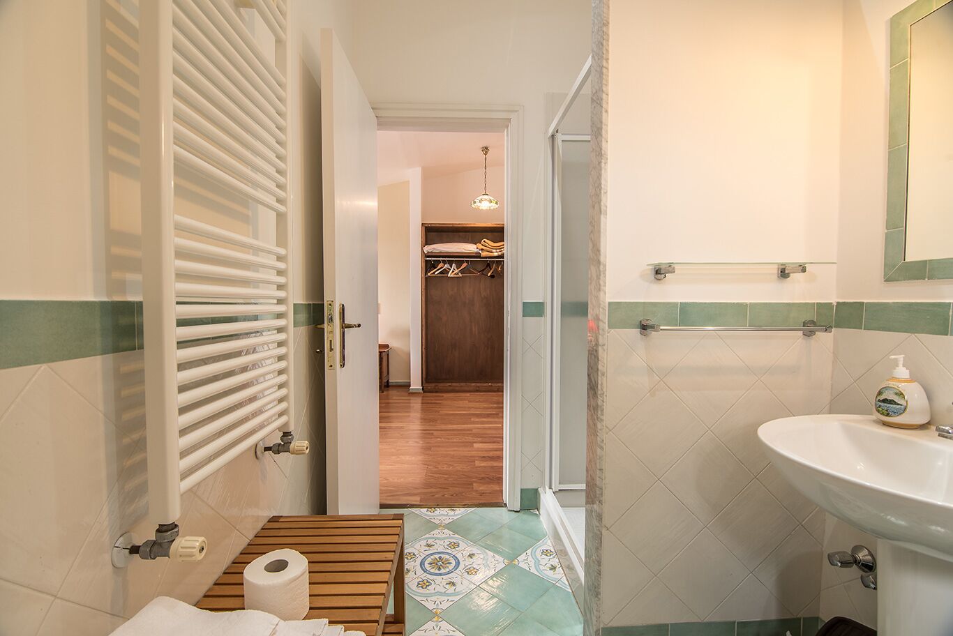 A bathroom with a toilet, sink, and shower area. There is a towel on the floor and a bottle of soap on the sink.