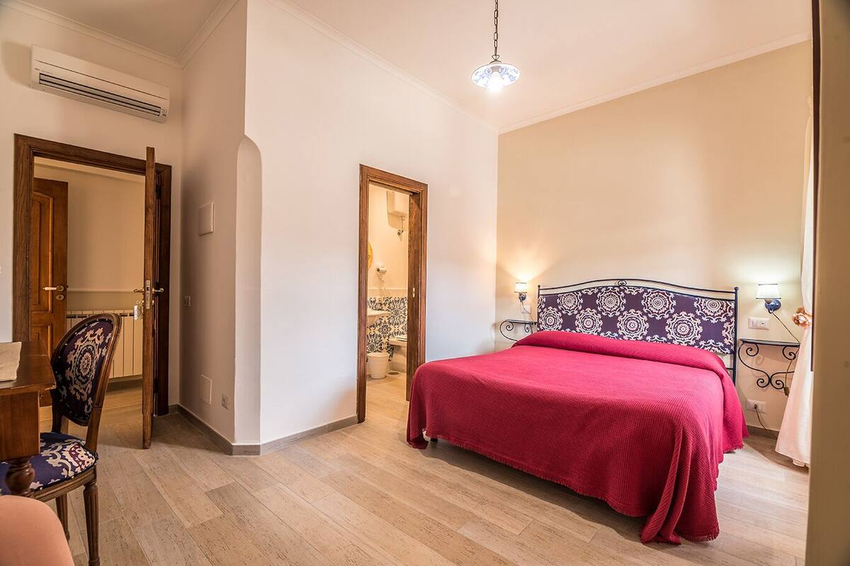 A bedroom with a bed, a chair, a desk, and an air conditioning unit.