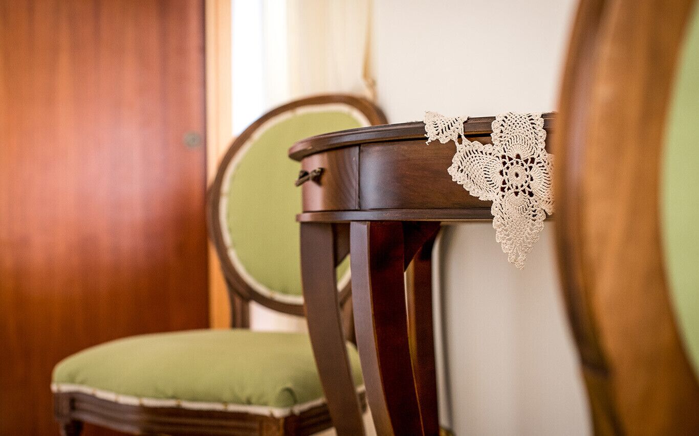 A wooden chair with a green cushion and a lace tablecloth.