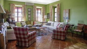 Un salon aux murs verts, avec un canapé, deux fauteuils à motifs écossais, une table basse et un piano.