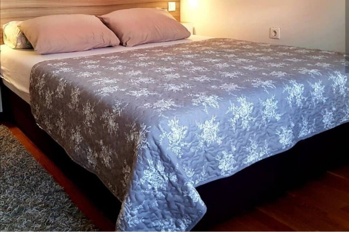 A bedroom with a wooden headboard, a bed with a floral-patterned bedspread, and a nightstand with a lamp.