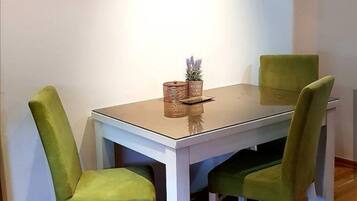 A dining table with four green upholstered chairs, a glass top, and a small plant on the table.