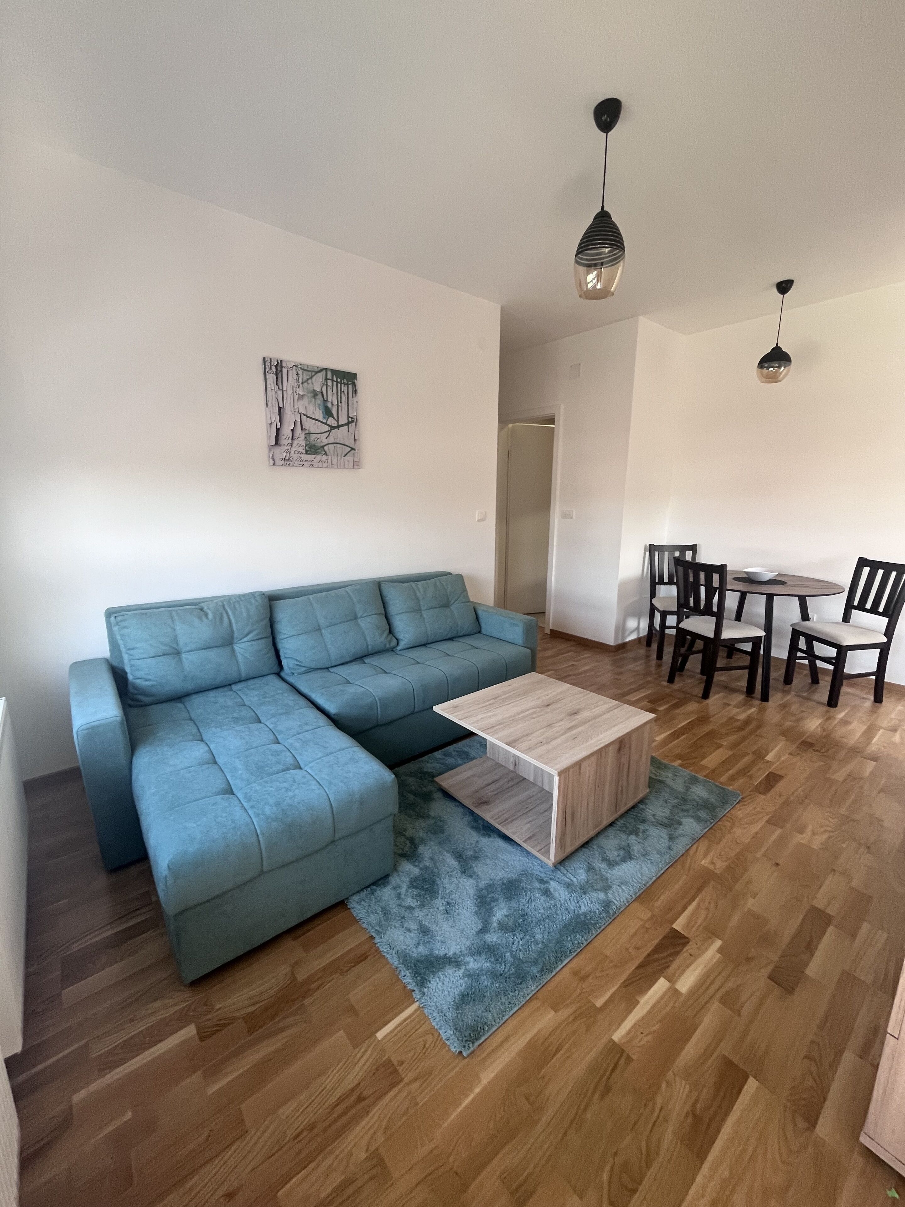 Ein Wohnzimmer mit einem blauen Ecksofa, einem Holztisch und einem Essbereich mit Tisch und Stühlen.