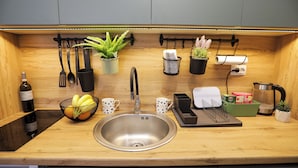 A modern kitchen with a stainless steel sink, wooden countertop, hanging utensils, potted plants, and a coffee maker. - Ana 2 (Banja Luka)