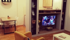A living room with a TV, a yellow armchair, a white coffee table, and a dining area with a table and chairs. - Ana 2 (Banja Luka)