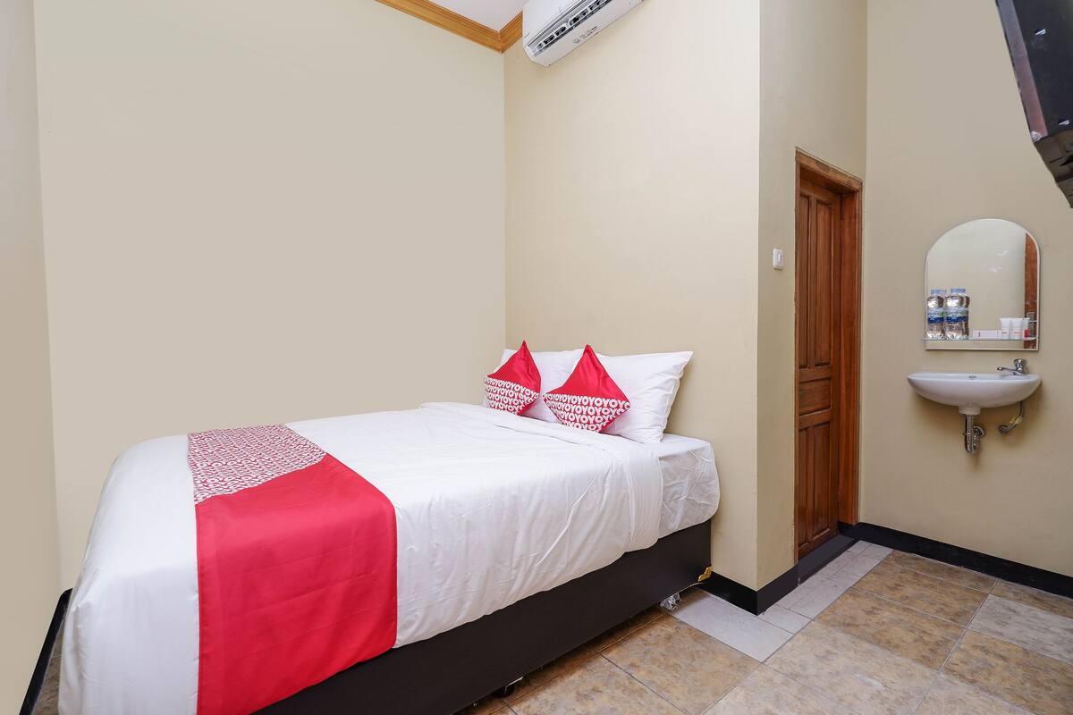 Une chambre à coucher avec un lit, une porte en bois, un lavabo fixé au mur et un appareil de climatisation.