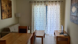 Un coin repas avec une table et des chaises en bois, un canapé et une lampe. Il y a une fenêtre avec des rideaux et un tableau au mur.
