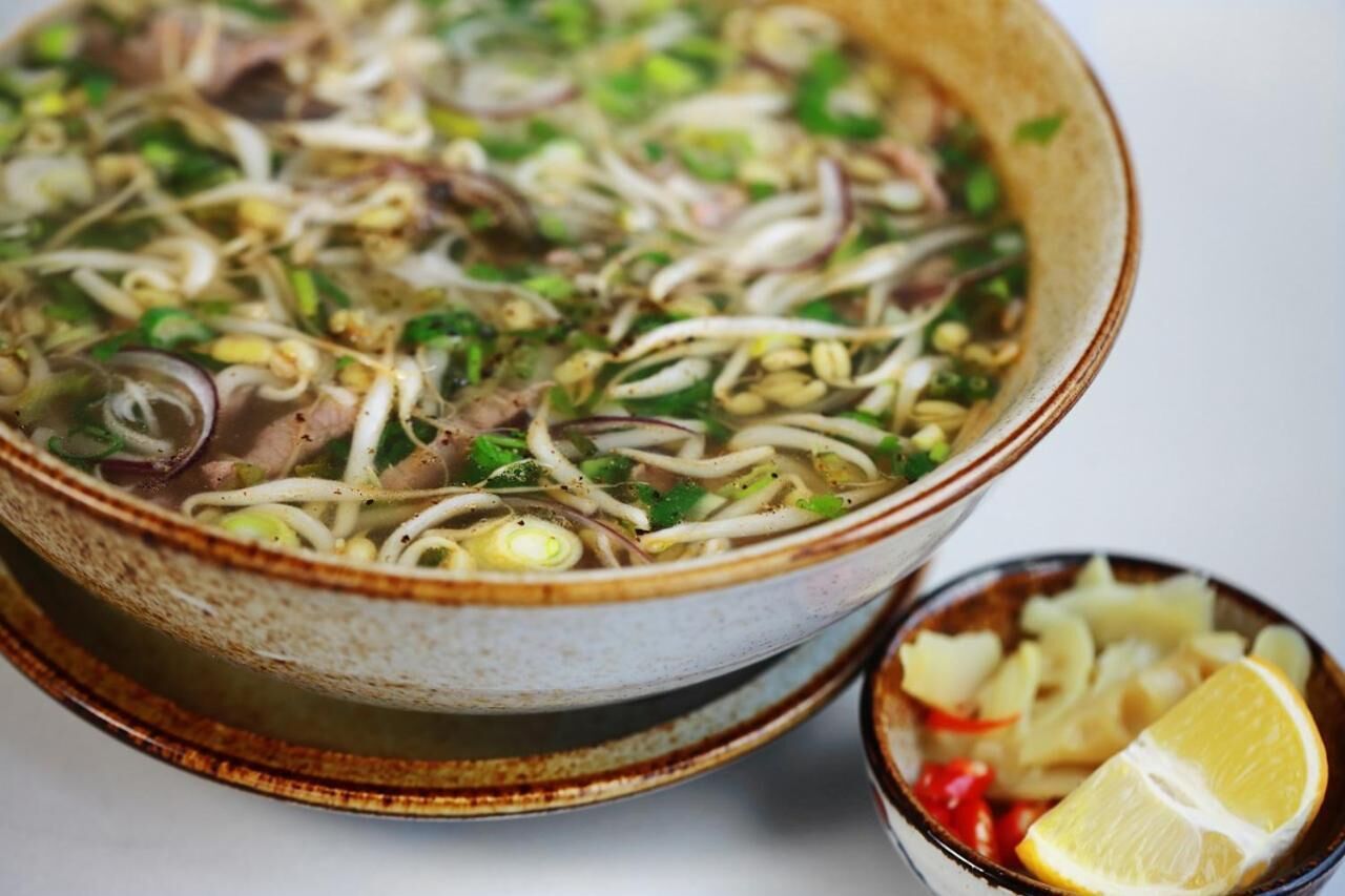 Un tazón de sopa de fideos con diferentes verduras y hierbas.