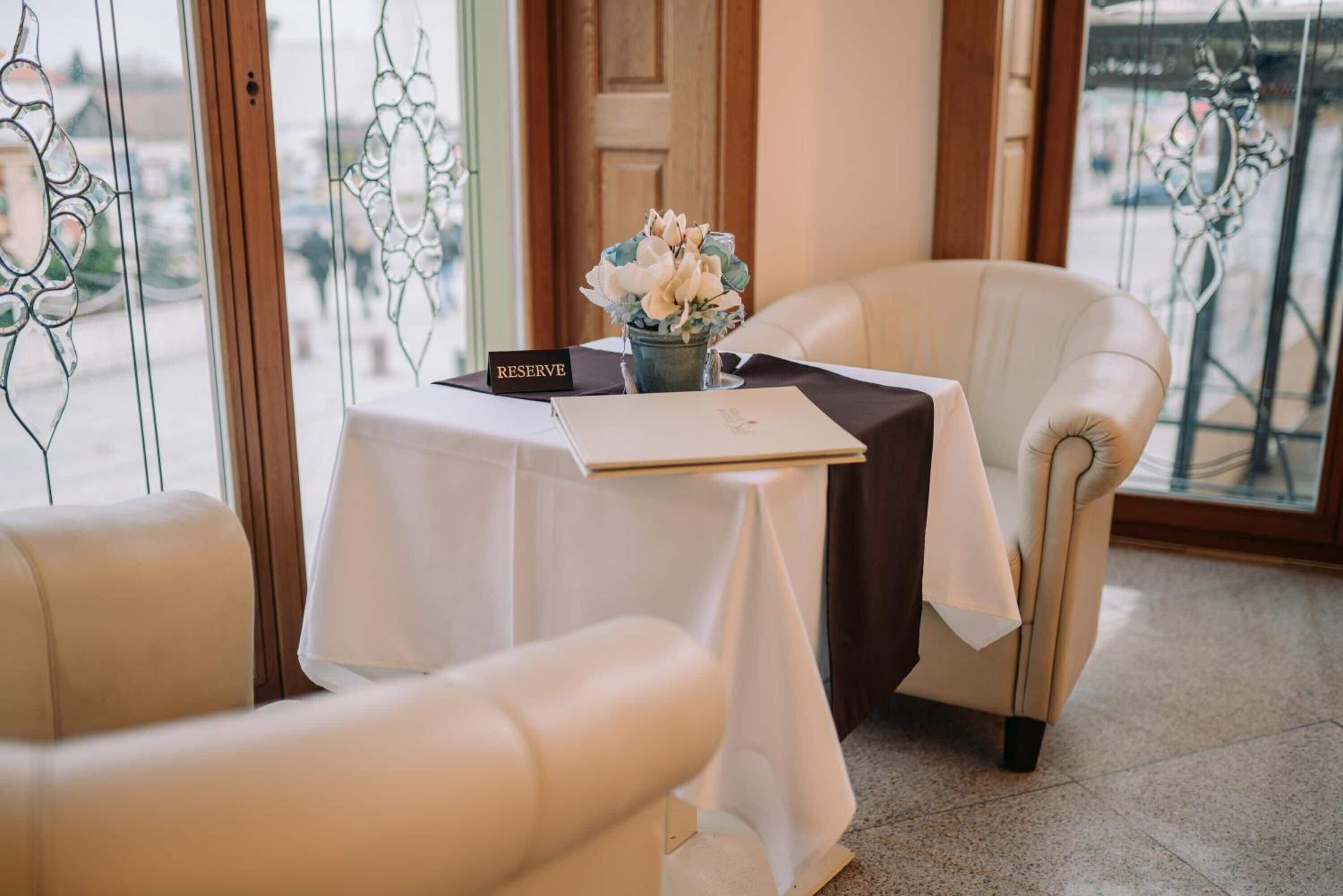 Habitación de hotel con una mesa preparada para dos, un cartel con la palabra 'RESERVE' y un jarrón de flores.