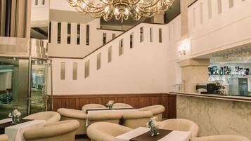 A spacious lobby with a grand chandelier, multiple seating areas, and a bar counter.
