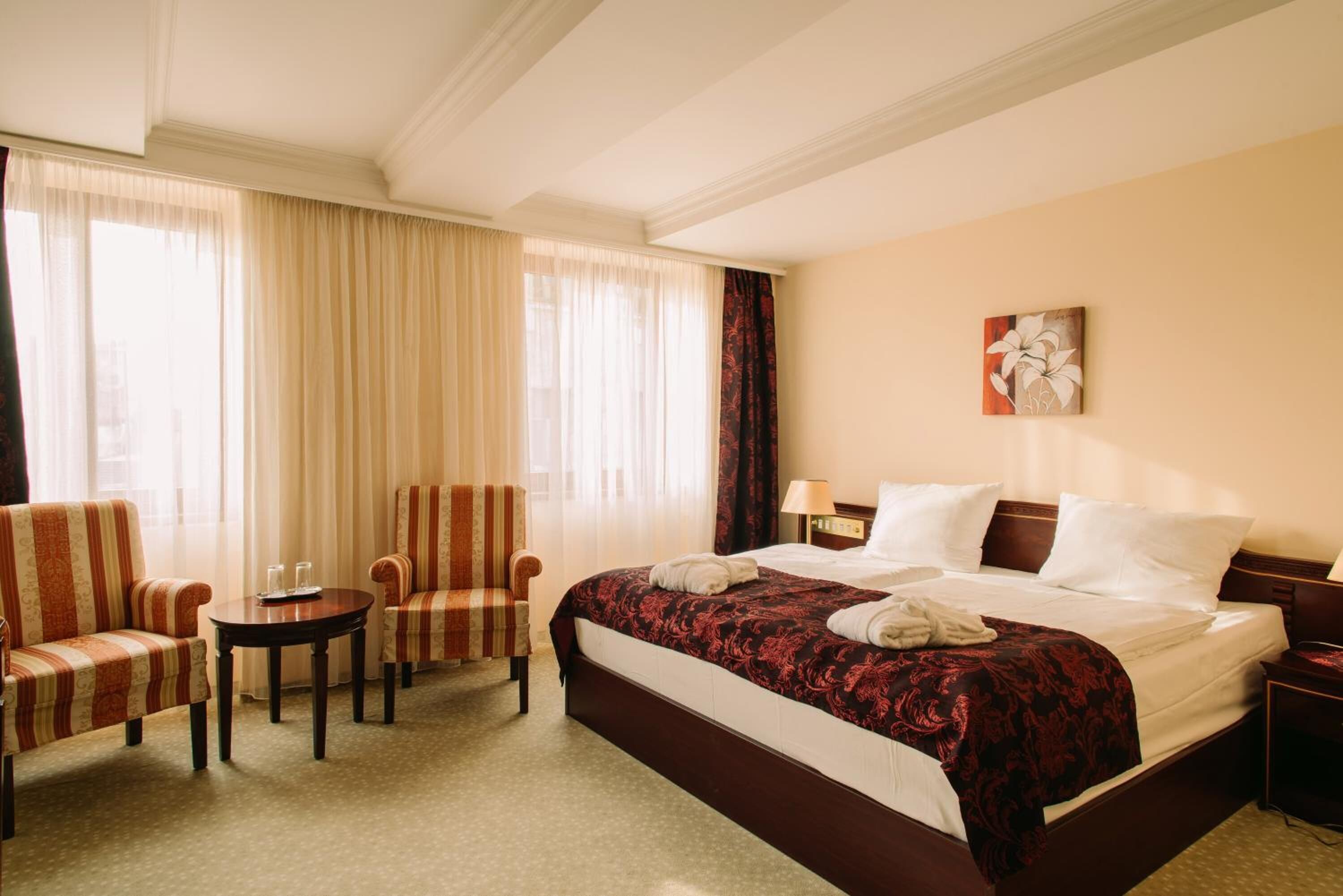 Ein Hotelzimmer mit einem großen Bett, zwei Sesseln, einem kleinen Tisch und einem Bild an der Wand.
