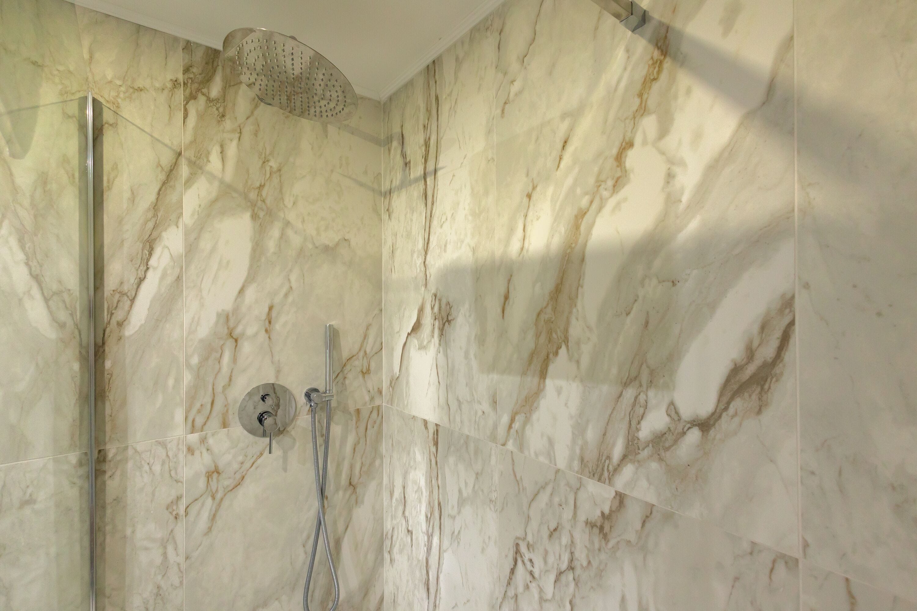 Baño con paredes de mármol y zona de ducha.