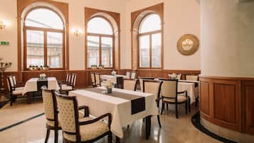 Zona pranzo con diversi tavoli e sedie, ampie finestre ad arco e un elemento decorativo a parete.