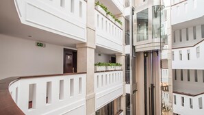 Un hôtel à plusieurs étages au design moderne, doté de balcons ornés de plantes, d’un ascenseur central et d’une décoration aux couleurs claires et épurées.