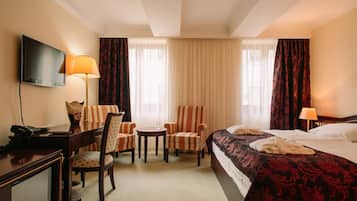 Une chambre d’hôtel comprenant un lit, deux fauteuils, une petite table, un bureau avec un téléphone et un téléviseur.