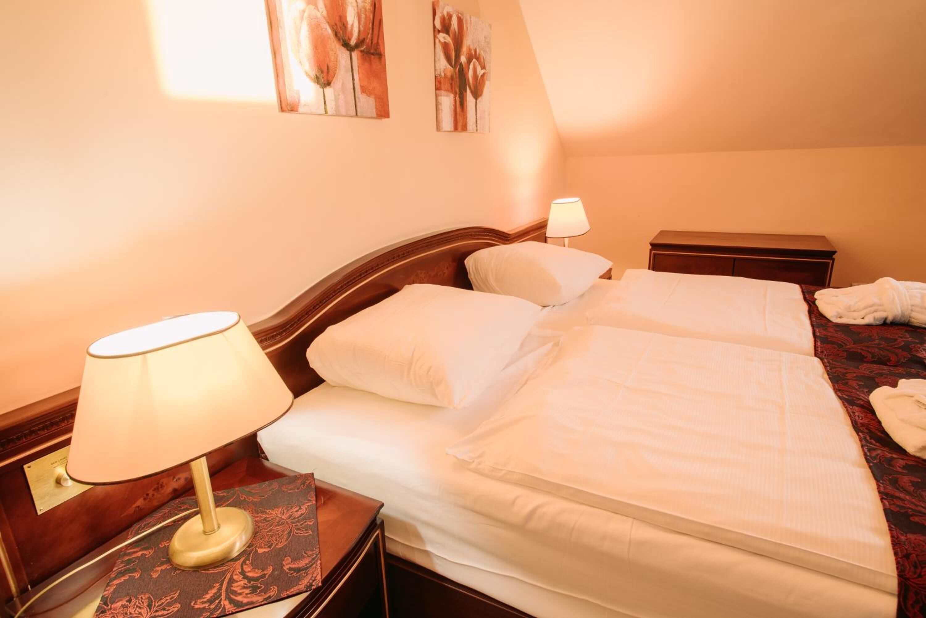 A double bed with white linens, a nightstand with a lamp, and a small bedside table.