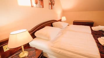A double bed with white linens, a nightstand with a lamp, and a small bedside table.