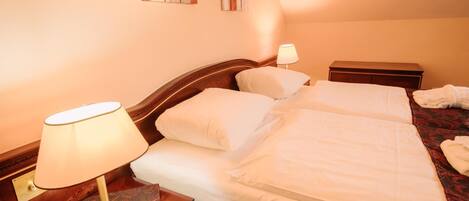 A double bed with white linens, a nightstand with a lamp, and a small bedside table.