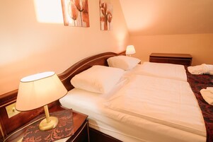 A double bed with white linens, a nightstand with a lamp, and a small bedside table.