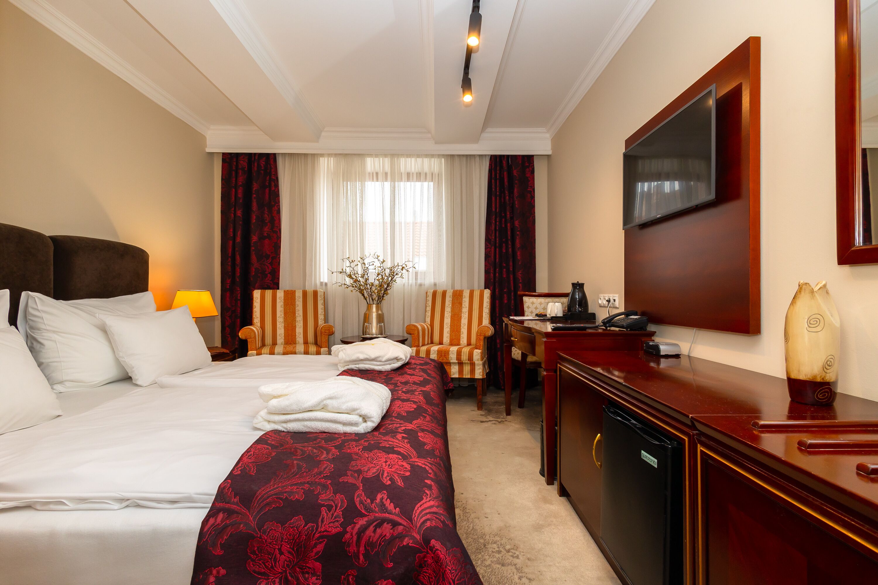 A hotel room with a large bed, a desk, a chair, a TV, and a minibar.
