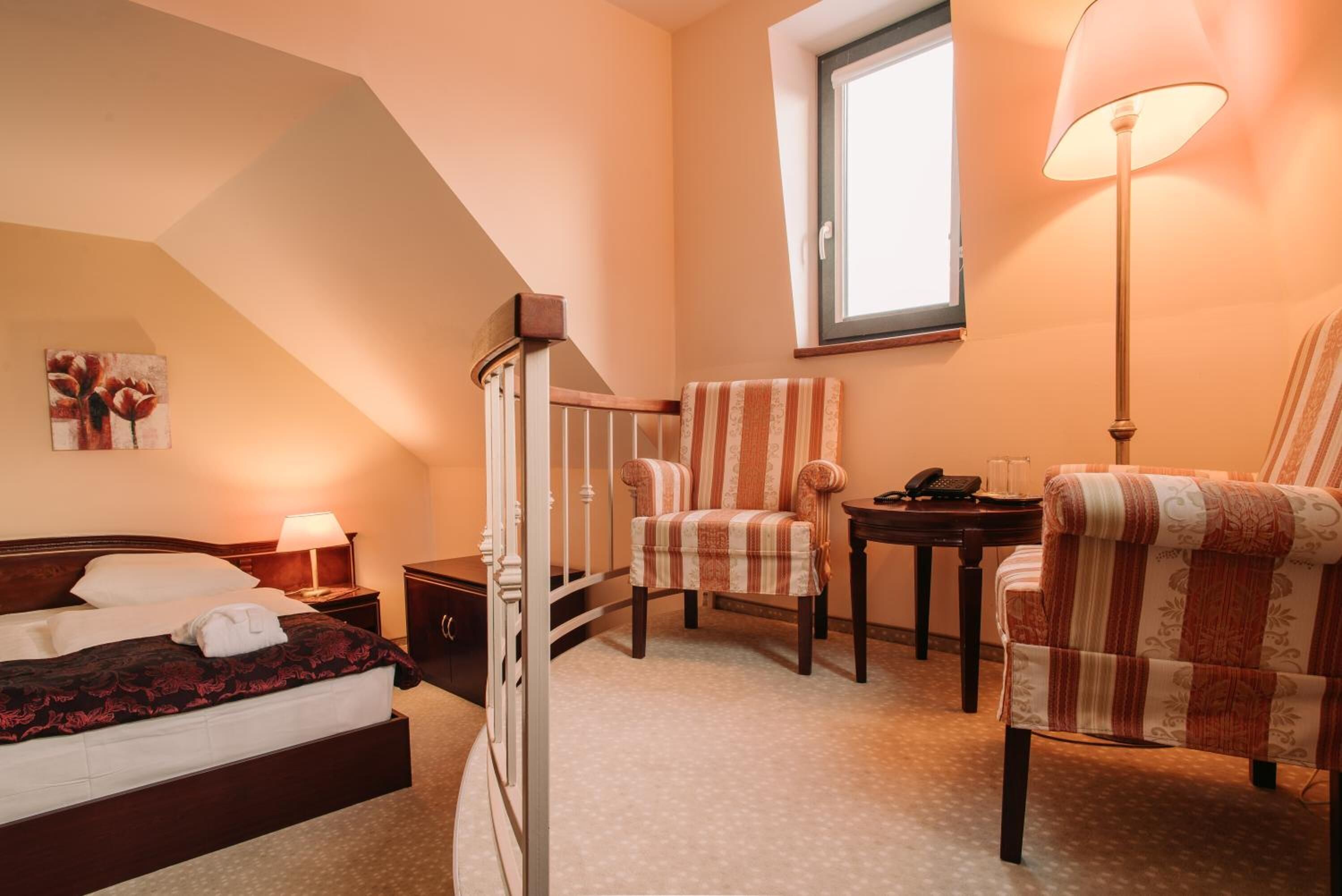 A bedroom with a bed, a chair, a desk, a lamp, and a painting on the wall.