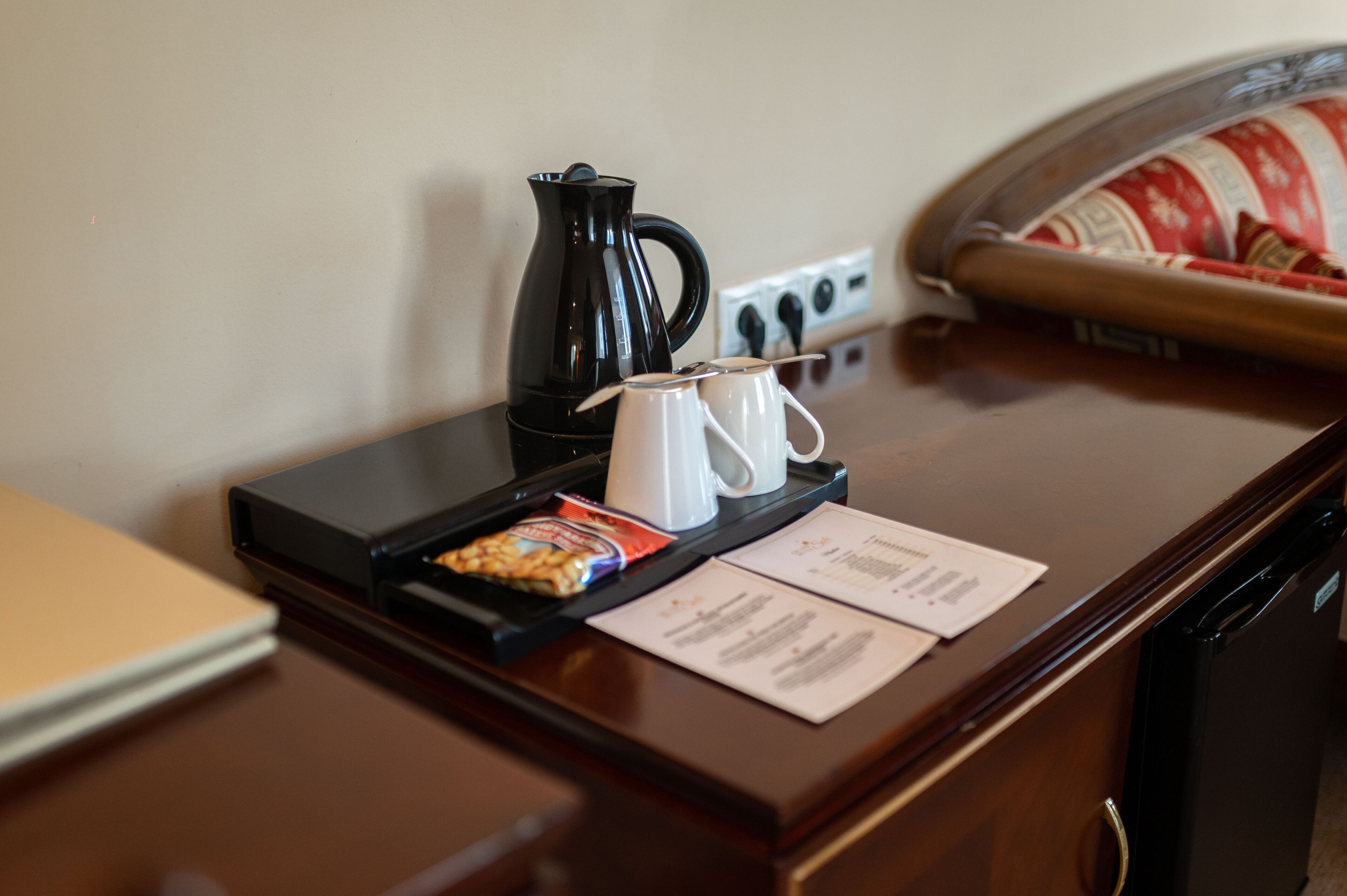 A hotel room desk with a coffee maker, two mugs, a tray with snacks, and a menu.