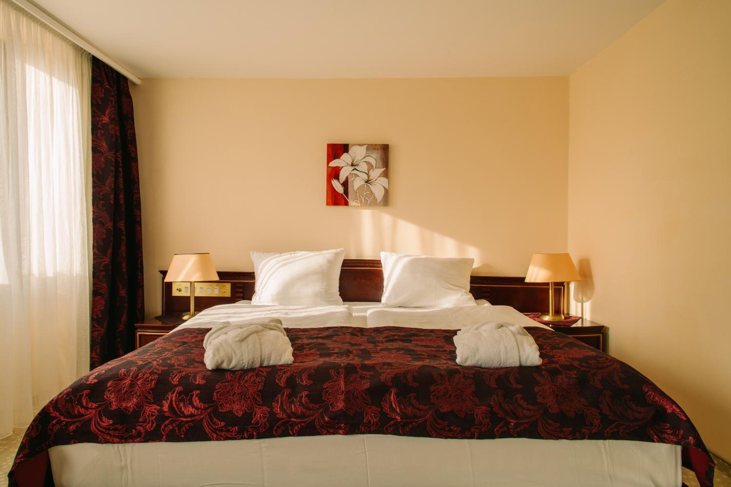 Une chambre d’hôtel avec un grand lit, deux lampes de chevet, un tableau au mur et une fenêtre avec des rideaux.