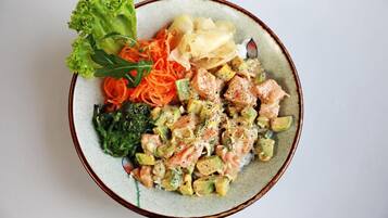 A bowl of food with salmon, vegetables, and a side salad.
