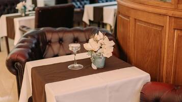 Een restaurantinterieur met lederen banken, witte tafellakens en een houten scheidingswand met een decoratief glasraam.