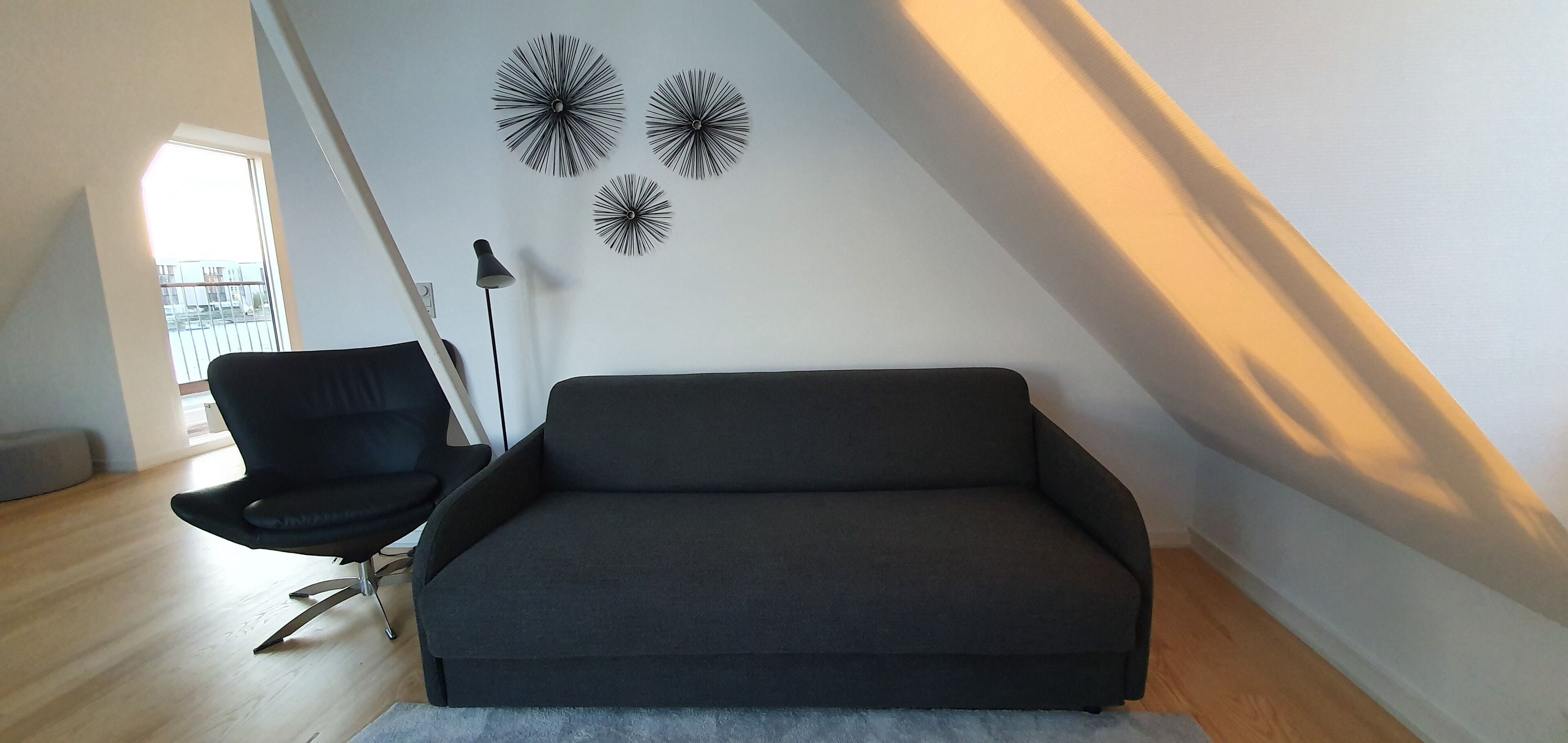 Un soggiorno moderno con un divano grigio scuro, una poltrona nera e tre elementi decorativi a parete.