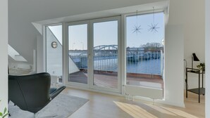 Et moderne værelse med store skydedøre, en sort stol, et lille bord og udsigt til en bro over vand.