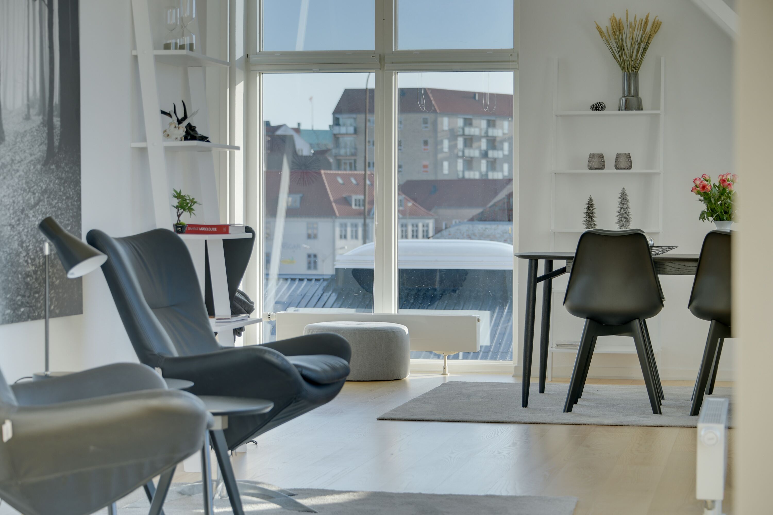Ein modernes Wohnzimmer mit großem Fenster, einem Essbereich mit Stühlen und einem Bücherregal mit Dekoration.