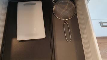 Uma gaveta de cozinha com uma tábua de corte branca e um escorredor de metal.