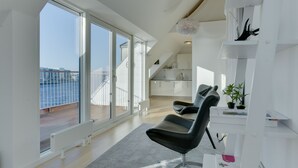 En moderne stue med en stor skydedør til en balkon, en sort læderstol og et hvidt reolsystem med dekorative genstande.