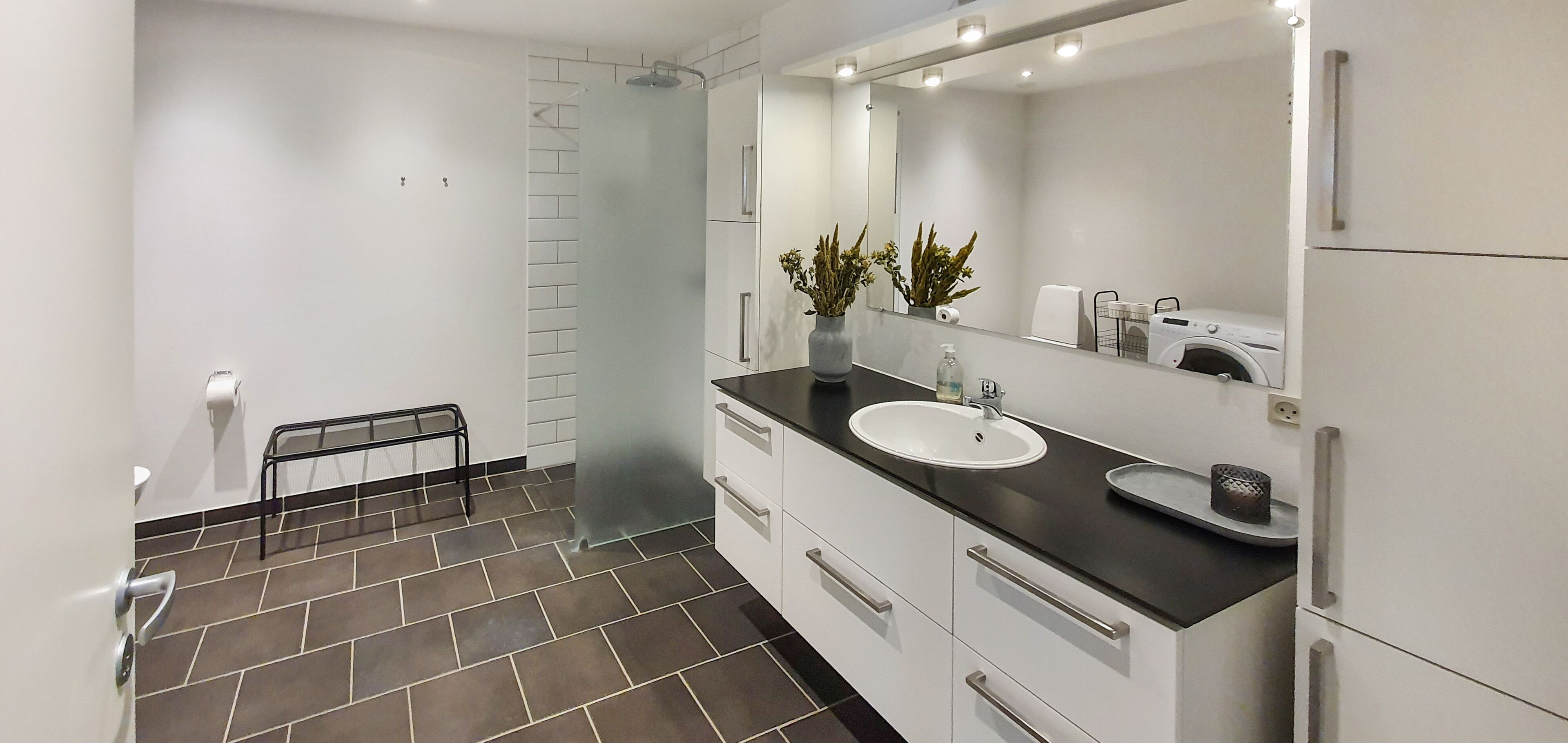 A modern bathroom with a white sink, dark countertop, and a large mirror.
