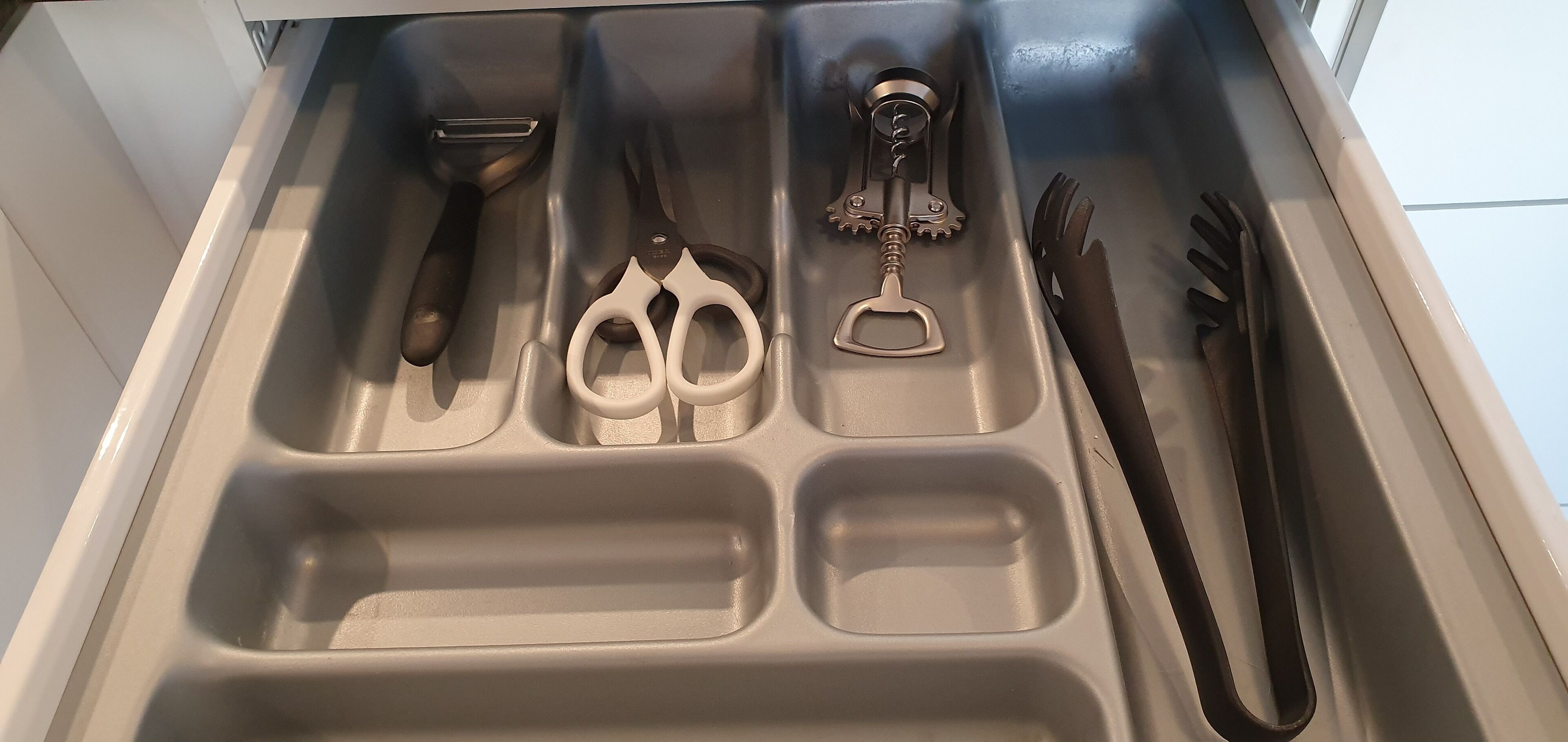 A drawer with a knife, scissors, and a corkscrew.