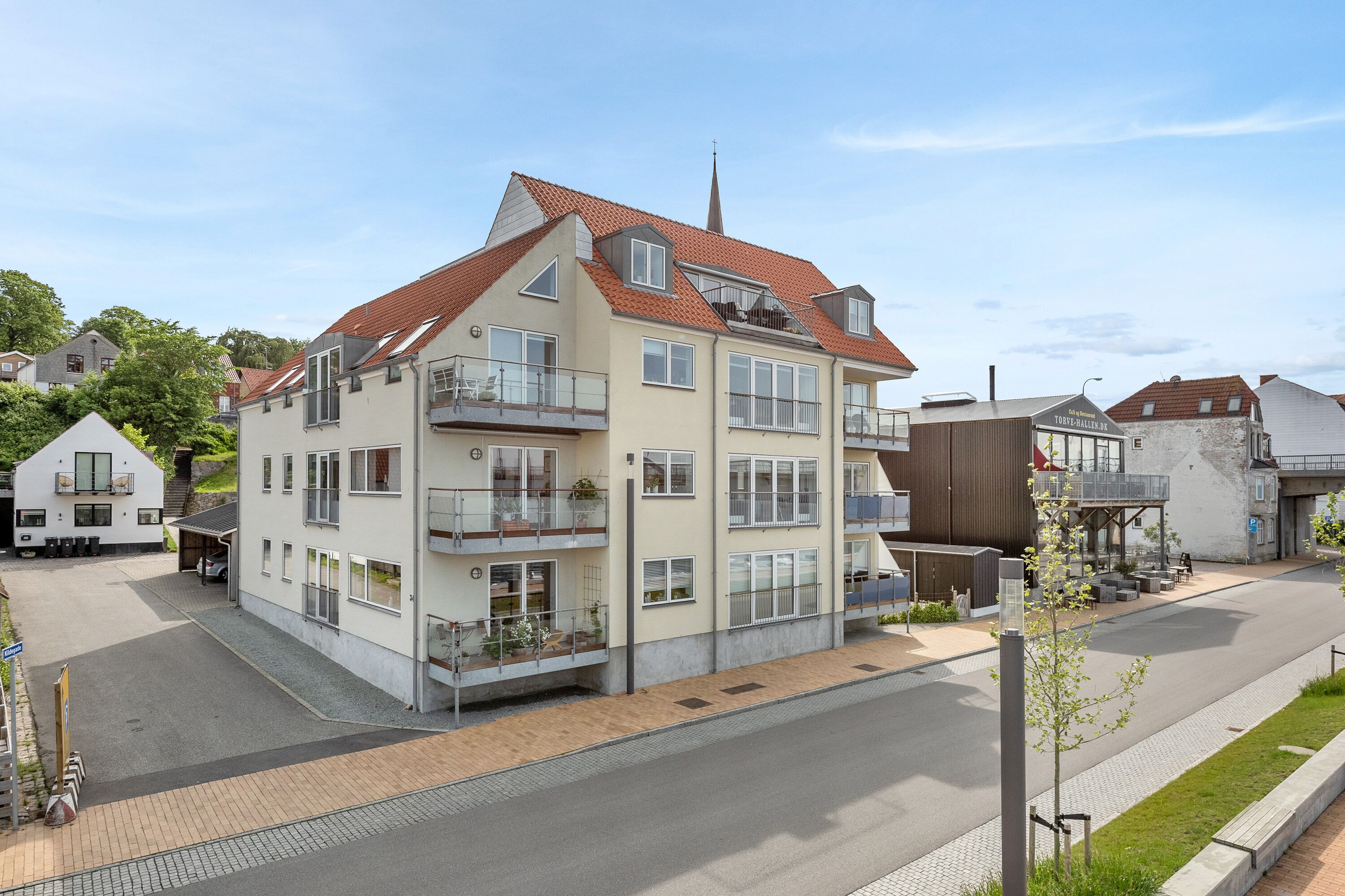 A multi-story building with balconies, a parking area, and a street view.