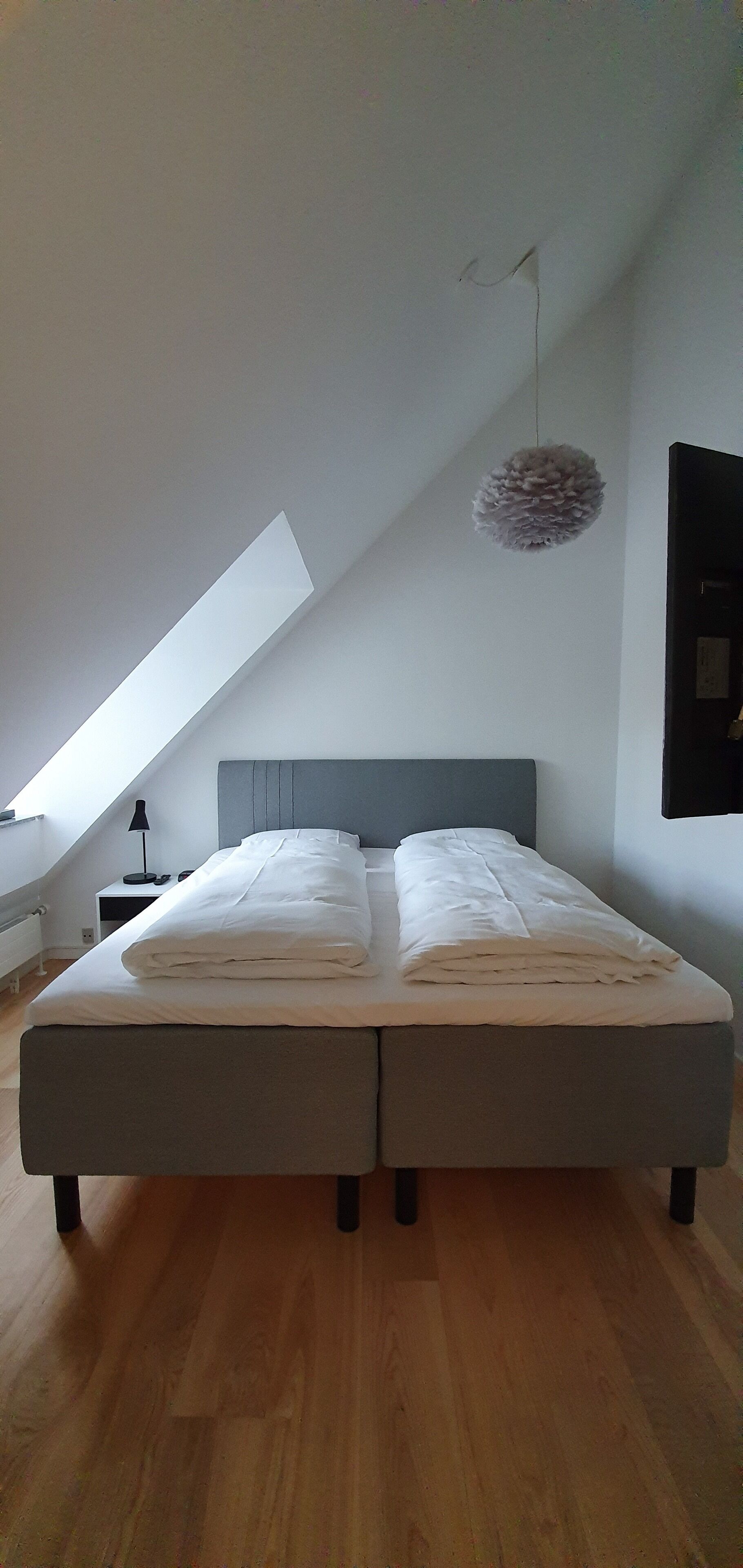 A modern bedroom with a large bed, a sloped ceiling, and a hanging light fixture.